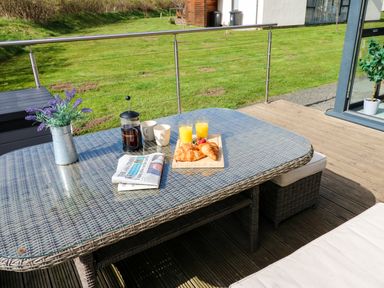 An outdoor patio with a wicker table set with croissants orange juice a French press two mugs a newspaper and a potted plant at Restharrow Lodge Bamburgh