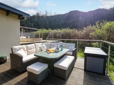 An outdoor seating area with cushioned wicker furniture and a glass table on a wooden deck at Restharrow Lodge in Bamburgh