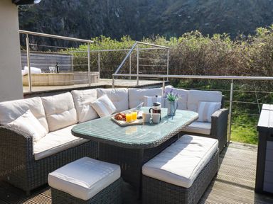 An outdoor patio seating area with a wicker sofa and table set on a wooden deck at Restharrow Lodge in Bamburgh