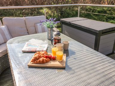 A glass table on a patio with croissants strawberries orange juice a coffee press mugs a newspaper and a vase with flowers at Restharrow Lodge in Bamburgh