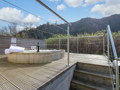 An outdoor wooden deck with a hot tub towels wine bottle and glasses overlooking a mountainous landscape at Restharrow Lodge in Bamburgh