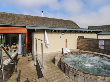An outdoor wooden deck with a round bubbling hot tub a bottle of wine two glasses and a white towel at Restharrow Lodge in Bamburgh