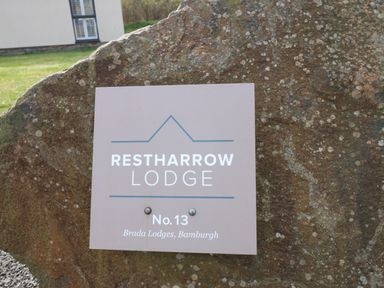 A stone with a Restharrow Lodge sign on it outside a building at Restharrow Lodge Bamburgh