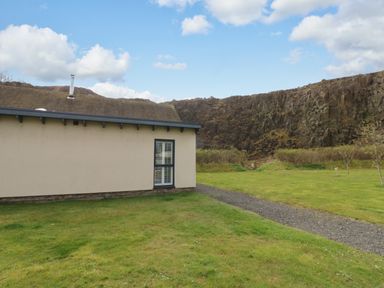 A side view of a building with a window and gravel path on a lawn with rocky hills in the background at Restharrow Lodge in Bamburgh