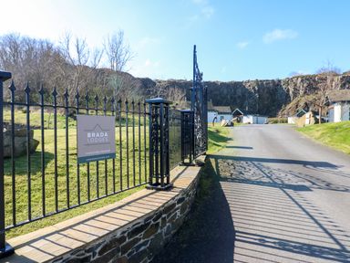 An entrance gate with a sign for Brada Lodges along a paved road leading to buildings at Brada Lodges in Bamburgh