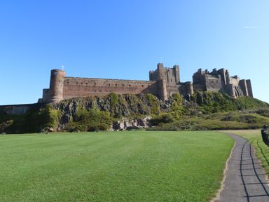A castle on a hill with grass and a pathway in front at Restharrow Lodge in Bamburgh