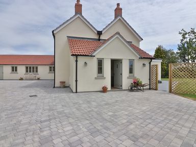 A paved driveway outside a cream house with a red tiled roof and wooden gates at The Retreat in Lympsham