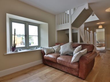 A living area with a leather sofa and cushions near a window with a plant and cups on the sill at The Retreat in Lympsham