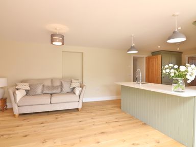 A living room area with a beige sofa and patterned cushions next to a kitchen island with flowers in a vase at The Retreat in Lympsham