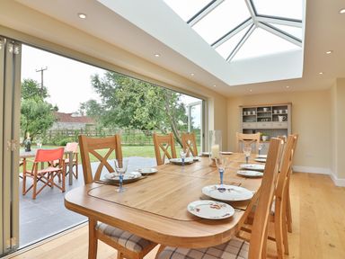 A dining room with a wooden table set with plates and glasses and a glass ceiling at The Retreat in Lympsham