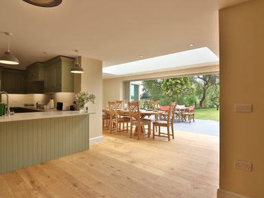 A kitchen with green cabinets and a dining area with wooden chairs and a table opening to a garden at The Retreat in Lympsham