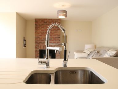 A kitchen sink with a modern faucet and a living room with a sofa and cushions at The Retreat in Lympsham