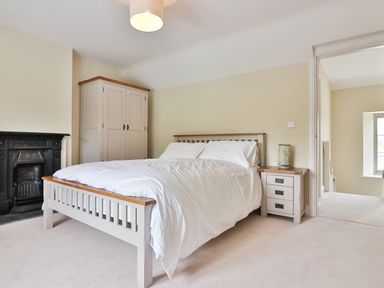 A bedroom with a bed white bedding a wardrobe bedside table lamp and a fireplace at The Retreat in Lympsham