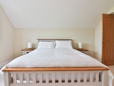 A bedroom with a bed white bedding two bedside tables and lamps and an open wooden door at The Retreat in Lympsham