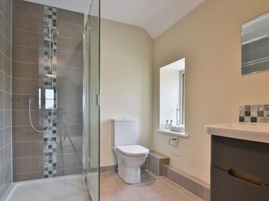 A bathroom with a shower cubicle a toilet a window and a sink with cabinet at The Retreat in Lympsham
