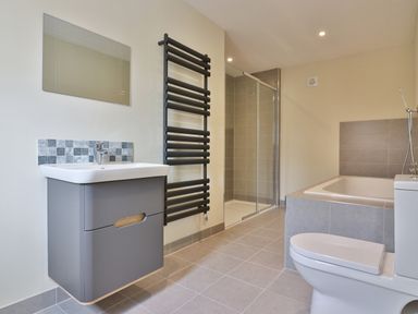 A bathroom with a wall-mounted sink, a mirror, a black towel radiator, a shower enclosure, a bathtub, and a toilet at The Retreat in Lympsham