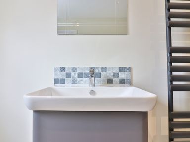 A bathroom sink with a faucet and patterned tile backsplash with a mirror above at The Retreat in Lympsham