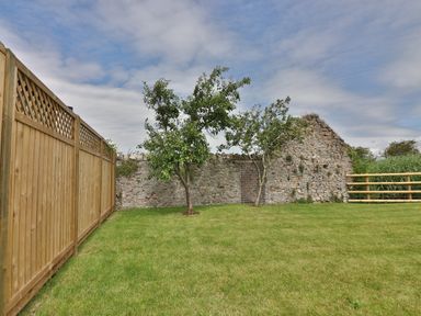 A garden with green grass two small trees a wooden fence on the left and a stone wall with a gate at The Retreat in Lympsham