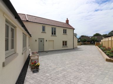 A paved driveway with a wooden bench and flower pots beside a cream house with grey framed windows at The Retreat in Lympsham