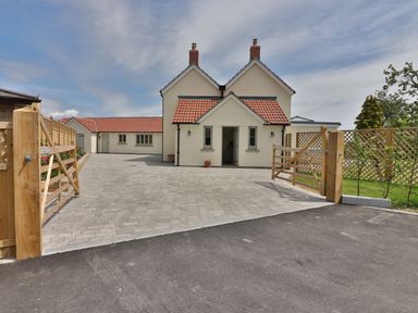 A house with red tiled roofs a paved driveway and wooden gates at the entrance at The Retreat in Lympsham