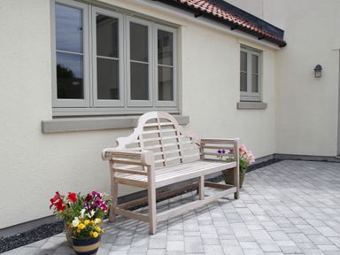 A wooden bench on a paved patio outside a house with two windows and flower pots nearby at The Retreat in Lympsham
