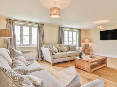 A living room with beige sofas wooden coffee table with bottle and glasses and wall mounted television at The Retreat in Lympsham