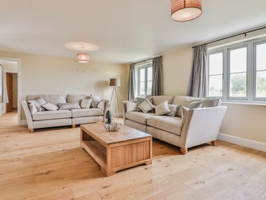 A living room with two sofas a wooden coffee table two windows with curtains and a floor lamp at The Retreat in Lympsham