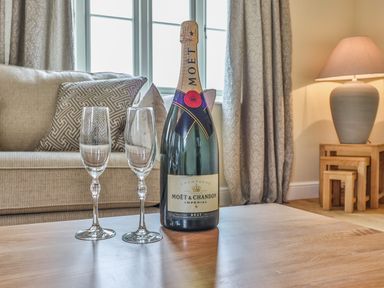 A bottle of Moet champagne with two empty glasses on a wooden table in a living room with a sofa and a lamp at The Retreat in Lympsham