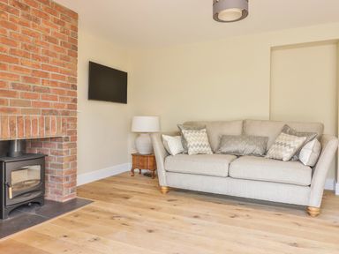 A living room with a beige sofa and a small wooden side table with a lamp next to a brick fireplace and a wall-mounted television at The Retreat in Lympsham