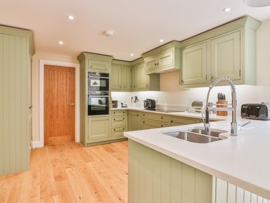 A kitchen with green cabinets wooden floor built in double oven and a sink with a flexible faucet at The Retreat in Lympsham