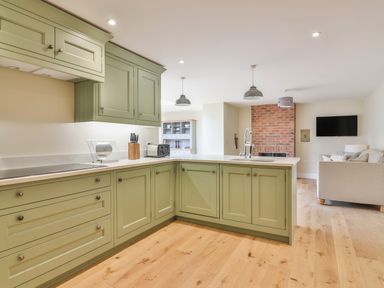 A kitchen area with green cabinets wooden floor and a living room with a beige sofa and a brick fireplace at The Retreat in Lympsham