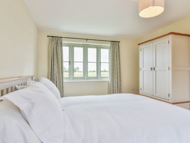 A bedroom with a bed white bedding window with curtains and a wardrobe at The Retreat in Lympsham