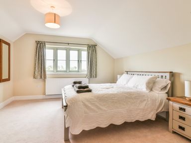 A bedroom with a bed with white bedding and towels on it a wooden nightstand with a lamp and a window with curtains at The Retreat in Lympsham