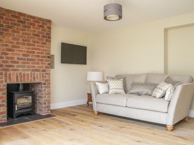 A living room with a beige sofa cushions wood burner and wall mounted tv at The Retreat in Lympsham