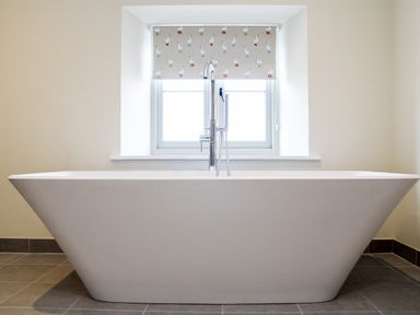 A bathroom with a freestanding bathtub in front of a window with a patterned blind at The Retreat in Lympsham