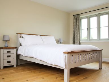 A bedroom with a bed with white bedding two bedside tables with lamps and a window with curtains at The Retreat in Lympsham