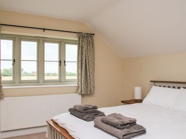A bedroom with a bed with white linens and folded towels on it next to a window with floral curtains at The Retreat in Lympsham