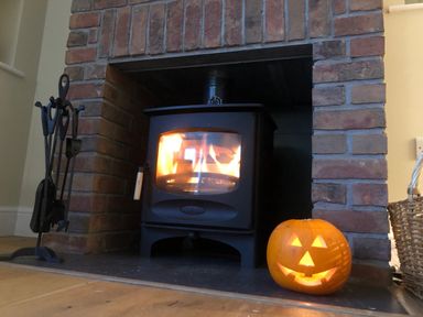 A wood burning stove with fire inside next to a carved pumpkin on a hearth at The Retreat in Lympsham