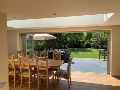 A dining area with wooden table and chairs opening to a garden with outdoor seating and umbrella at The Retreat in Lympsham