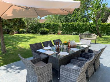 An outdoor patio with a dining table set with plates and glasses under a large umbrella at The Retreat in Lympsham
