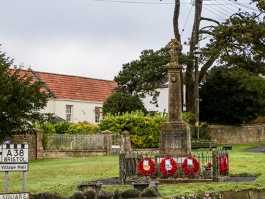 A war memorial with poppy wreaths near a road sign for A38 Bristol and Village Hall in a village