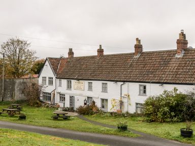 A white building with a tiled roof and chimneys with picnic tables on the grass in front at Stable Cottage in Shipham
