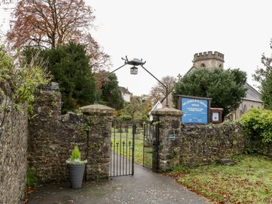 The entrance gate to The Church of St Leonard with stone walls and a blue sign at Stable Cottage in Shipham