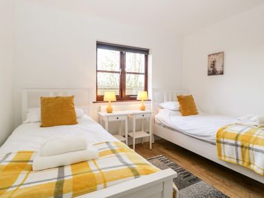 A bedroom with two single beds a window two bedside tables with lamps and folded towels at Stable Cottage in Shipham
