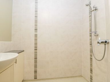 A bathroom with a sink cabinet and a shower with tiled walls and a narrow vertical decorative tile strip at Stable Cottage in Shipham