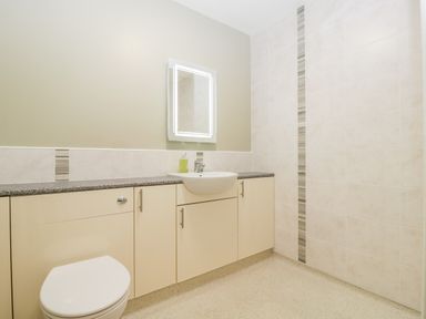 A bathroom with a toilet sink cabinets and a lighted mirror at Stable Cottage in Shipham