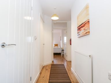 A hallway with a striped rug wooden floor white doors and walls a radiator and a painting at Stable Cottage Shipham