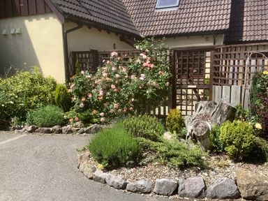 A garden with various plants and flowers in front of a house with a tiled roof and lattice fence at Stable Cottage in Shipham