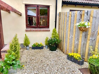 A small garden area with gravel ground plants in pots and flower boxes and a hanging flower basket at Stable Cottage in Shipham