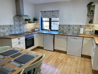 A kitchen with wooden flooring wooden countertops white cabinets a dining table with placemats and chairs at Stable Cottage in Shipham